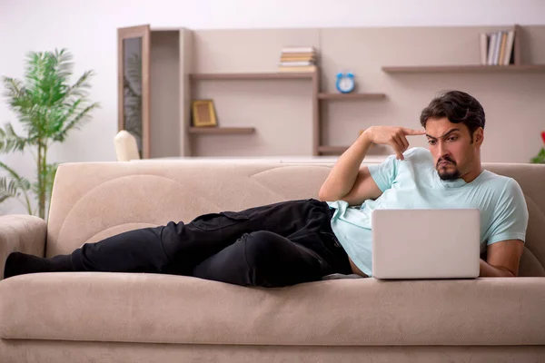 Jovem sentado no sofá com computador em casa — Fotografia de Stock