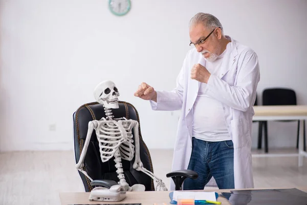 Vieux médecin masculin avec squelette à la clinique — Photo