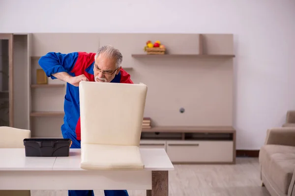 Oude mannelijke timmerman repareert stoel binnen — Stockfoto