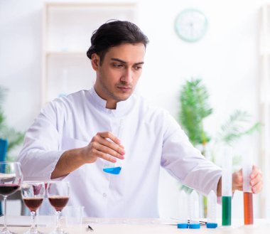 Erkek kimyager laboratuvarda şarap örneklerini inceliyor.
