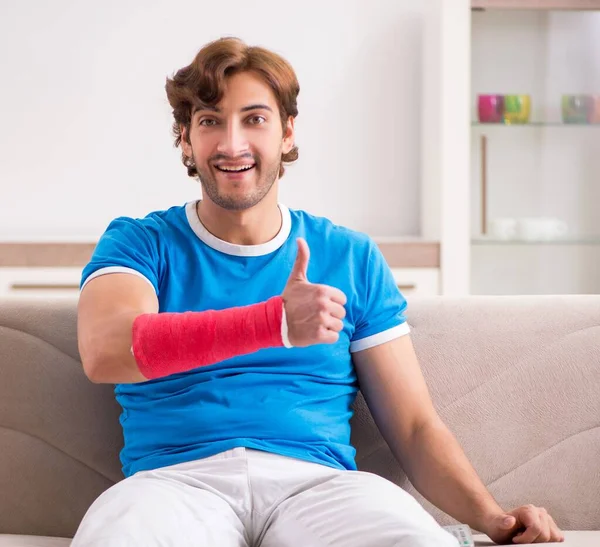 Молодой человек с поврежденной рукой сидит на диване — стоковое фото