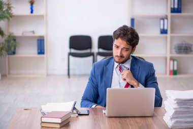 Genç bir erkek çalışan ve ofiste çok fazla iş var.