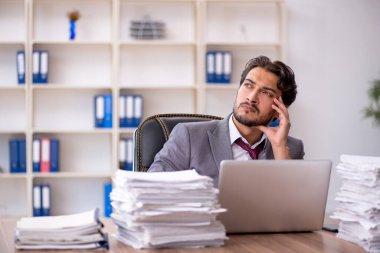 Genç bir erkek çalışan ve ofiste çok fazla iş var.