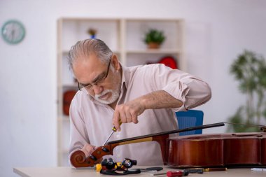 Yaşlı erkek tamirci atölyede müzik aletlerini tamir ediyor.