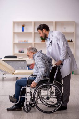 Tekerlekli sandalyedeki yaşlı adam genç erkek doktoru ziyaret ediyor.
