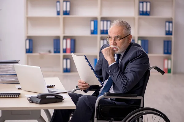 Homem velho empregado em cadeira de rodas sentado no local de trabalho — Fotografia de Stock