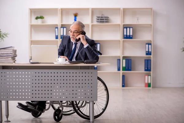 Oude mannelijke werknemer in rolstoel zittend op de werkplek — Stockfoto