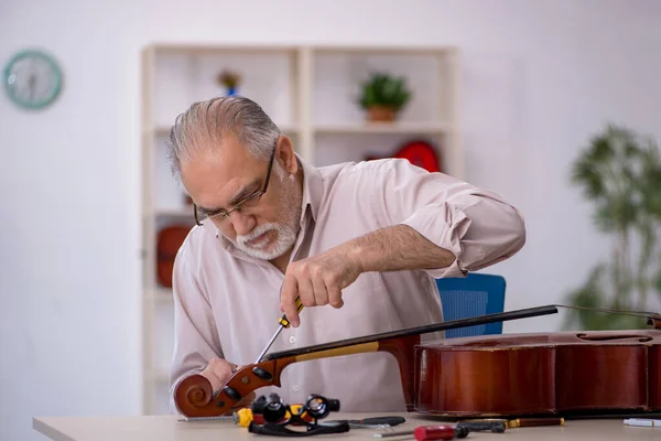 Homem velho reparador reparando instrumentos musicais na oficina — Fotografia de Stock