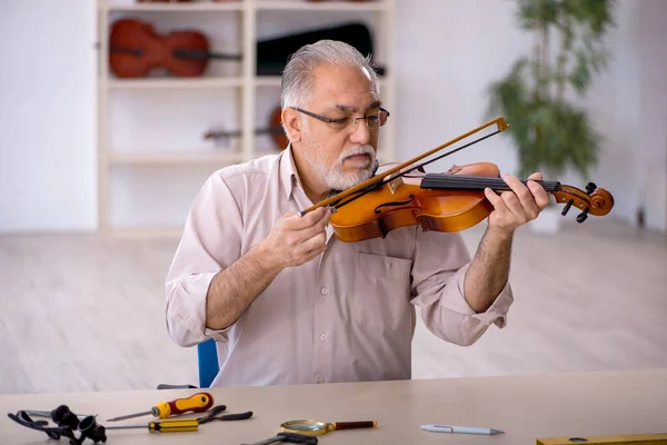 Oude mannelijke reparateur repareert muziekinstrumenten in werkplaats — Stockfoto