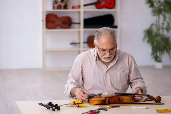Viejo reparador masculino reparando instrumentos musicales en el taller — Foto de Stock