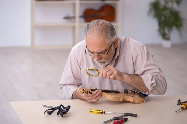 Старый мастер по ремонту музыкальных инструментов в мастерской — стоковое фото