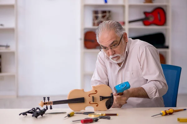 Old male repairman repairing musical instruments at workshop — Stock Photo, Image