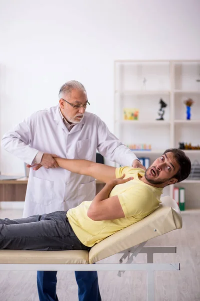 Genç erkek hasta yaşlı erkek doktor masörünü ziyaret ediyor. — Stok fotoğraf