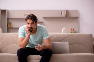 Genç adam evde televizyon izliyor.