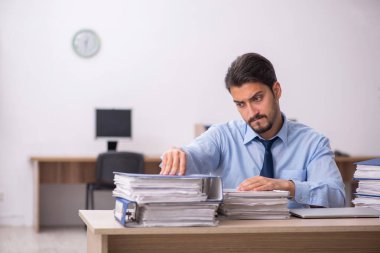 Genç bir erkek çalışan ve ofiste çok fazla iş var.