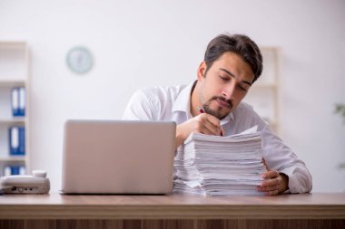 Genç bir erkek çalışan ve ofiste çok fazla iş var.