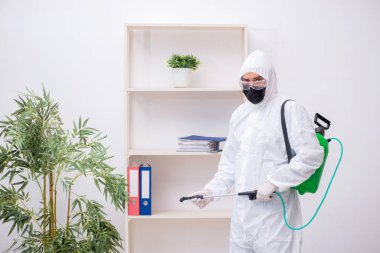 Young male contractor disinfecting office during pandemic