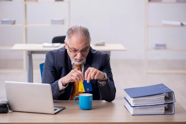 Старый работник мужского пола держит кредитную карту в офисе — стоковое фото