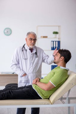 Genç erkek hasta yaşlı erkek doktoru ziyaret ediyor.