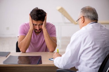 Genç erkek hasta yaşlı erkek doktoru ziyaret ediyor.