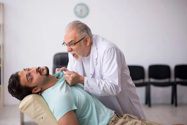 Junge männliche Patientin besucht alten männlichen Arzt — Stockfoto