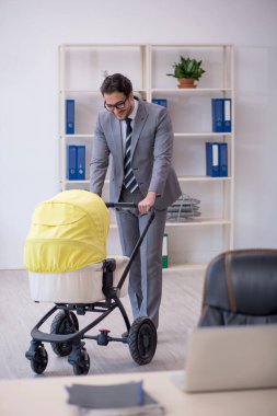 Genç erkek çalışan işyerinde yeni doğan çocuğa bakıyor.