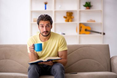 Genç adam salgın sırasında evde kitap okuyor.