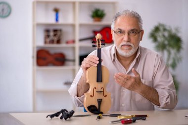 Yaşlı erkek tamirci atölyede müzik aletlerini tamir ediyor.
