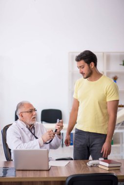 Genç erkek hasta yaşlı erkek doktoru ziyaret ediyor.