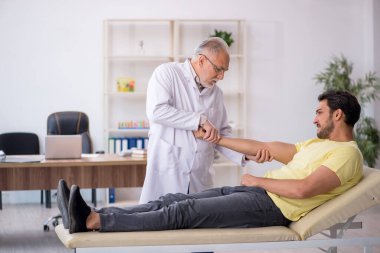Genç erkek hasta yaşlı erkek doktor masörünü ziyaret ediyor.