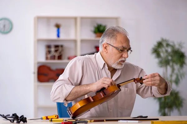 Oude mannelijke reparateur repareert muziekinstrumenten in werkplaats — Stockfoto