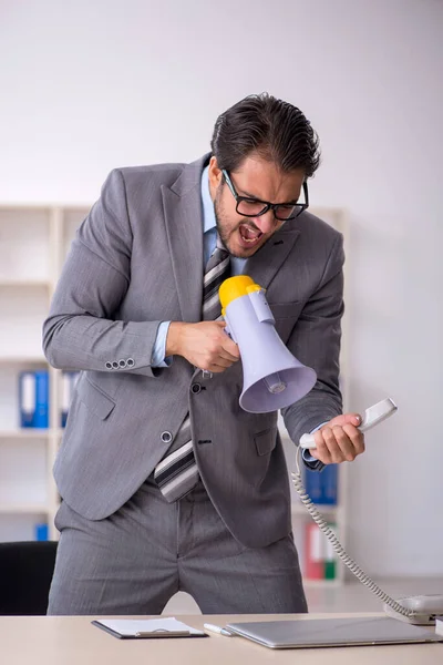 Молодой работник мужского пола держит мегафон в офисе — стоковое фото