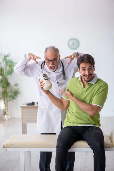 Jonge mannelijke patiënt bezoekt oude mannelijke arts in dure geneeskunde — Stockfoto