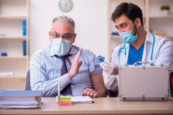 Junger Arzt besucht alten Geschäftsmann am Arbeitsplatz — Stockfoto