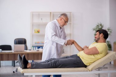 Genç erkek hasta yaşlı erkek doktor masörünü ziyaret ediyor.