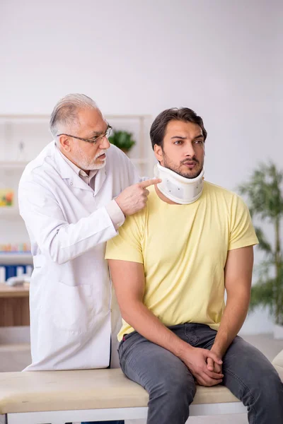 Junge männliche Nackenverletzung Patient besucht alten männlichen Arzt — Stockfoto
