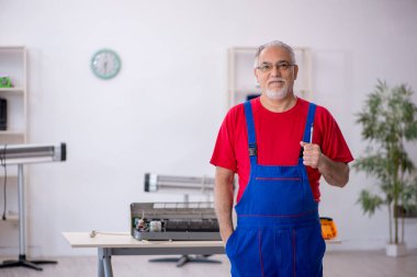 Eski tamirci atölyedeki klimayı tamir ediyor.