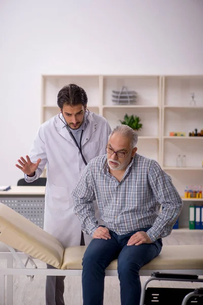 Tekerlekli sandalyedeki yaşlı adam genç erkek doktoru ziyaret ediyor.
