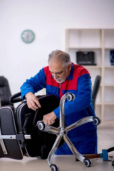 Stary mężczyzna naprawiający krzesło biurowe — Zdjęcie stockowe