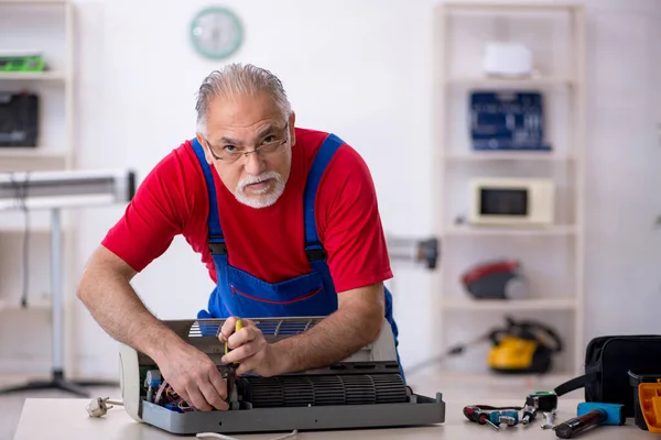 Reparador antigo reparando ar-condicionado na oficina — Fotografia de Stock