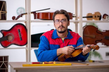 Genç adam atölyede müzik aletlerini tamir ediyor.