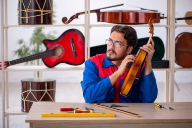 Genç adam atölyede müzik aletlerini tamir ediyor.