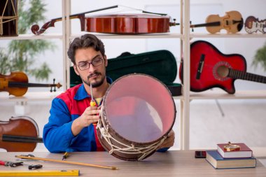 Genç adam atölyede müzik aletlerini tamir ediyor.