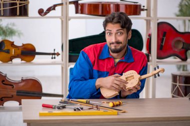 Genç adam atölyede müzik aletlerini tamir ediyor.