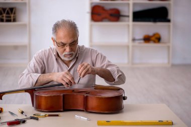 Yaşlı erkek tamirci atölyede müzik aletlerini tamir ediyor.