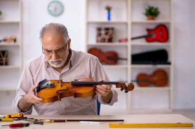 Yaşlı erkek tamirci atölyede müzik aletlerini tamir ediyor.