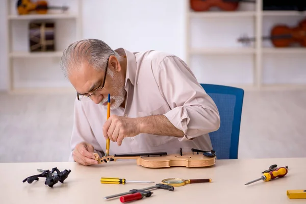 Старый мастер по ремонту музыкальных инструментов в мастерской — стоковое фото