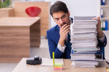 Genç bir erkek çalışan ve ofiste çok fazla iş var.