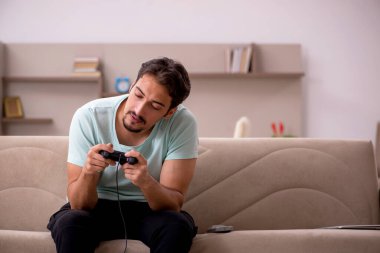 Genç adam evde joystick oynuyor.