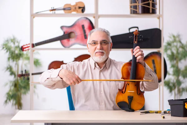 Old male repairman repairing musical instruments at workplace — Stock Photo, Image